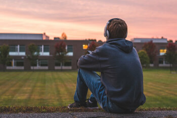 Ein Junge sitzt allein auf einer Wiese und hört Musik.