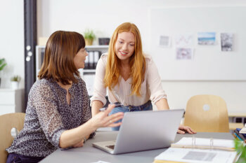 Eine ältere Dame und eine jugendliche Frau schauen auf einen Pc.