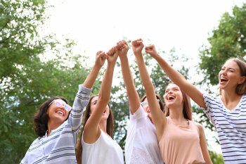 Vier junge Frauen recken gemeinsam die Fäuste in die Luft und lachen dabei.