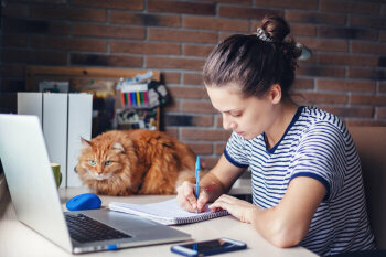 Eine junge Frau sitzt am Schreibtisch neben ihrer Katze.