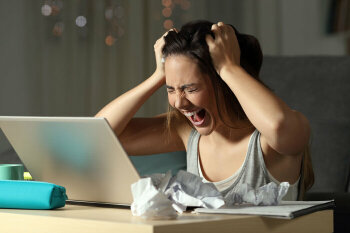 Ein junges Mädchen sitzt am Schreibtisch vor ihrem Laptop, rauft sich die Haare und schreit laut.
