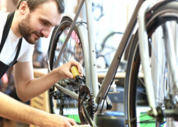 Ein Mann kniet neben einem Fahrrad und hält eine Öl-Tube an die Kette. 