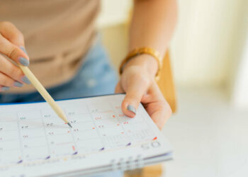Eine Frau hält einen Kalender in den Händen und deutet mit einem Stift auf ein Datum.