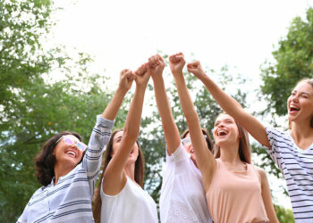 Vier junge Frauen recken gemeinsam die Fäuste in die Luft und lachen dabei.