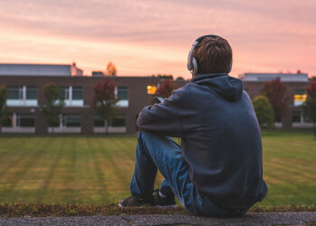 Ein Junge sitzt allein auf einer Wiese und hört Musik.