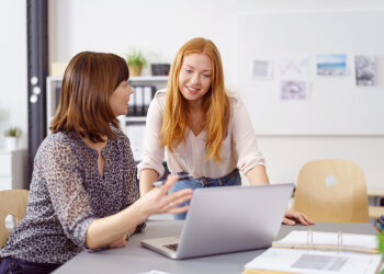 Eine ältere Dame und eine jugendliche Frau schauen auf einen Pc.