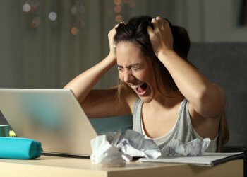 Ein junges Mädchen sitzt am Schreibtisch vor ihrem Laptop, rauft sich die Haare und schreit laut.