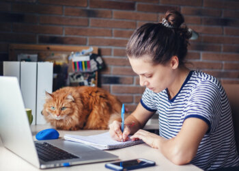 Eine junge Frau sitzt am Schreibtisch neben ihrer Katze