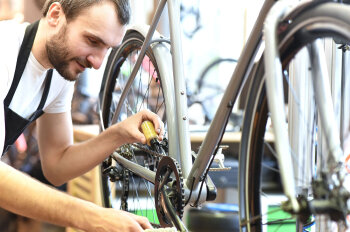 Ein Mann kniet neben einem Fahrrad und hält eine Öl-Tube an die Kette. 