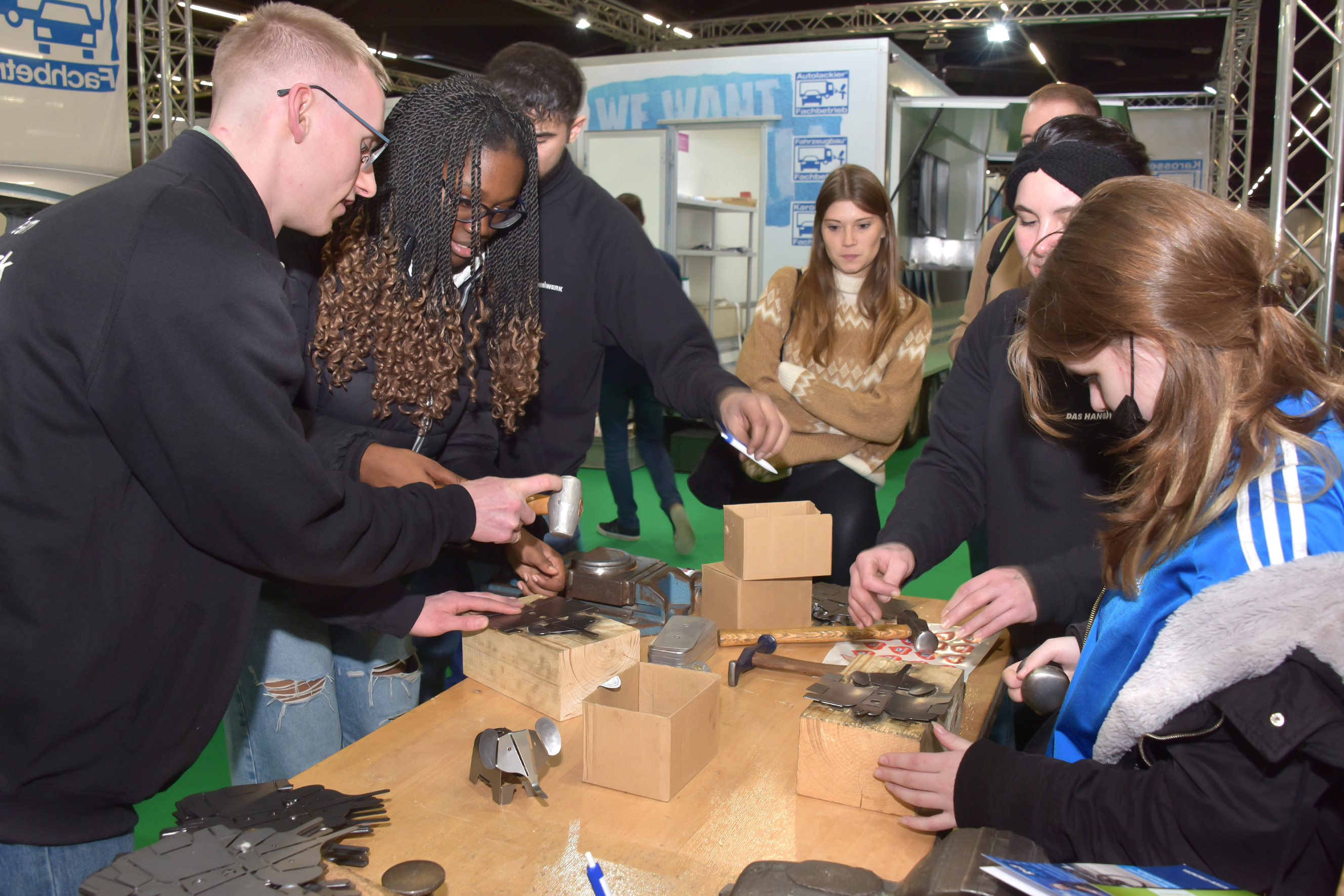 An einem Messestand stehen mehrere Jugendliche und probieren sich in kleinen Metallarbeiten aus.