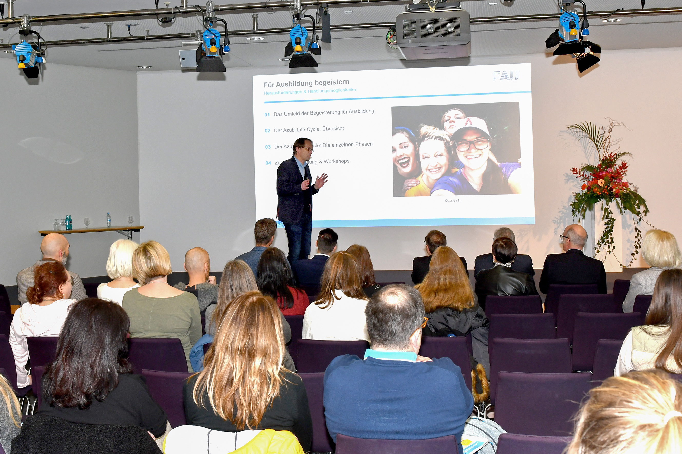 Mehrere Personen sitzen in einem Vortragssaal. Der Vortragende hält eine Powerpoint-Präsentation zum Thema "Für Ausbildung begeistern".