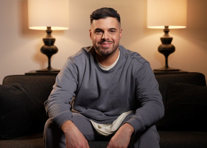 Auf einem Sofa sitzt ein junger Mann (Karim Jamal) und lächelt.