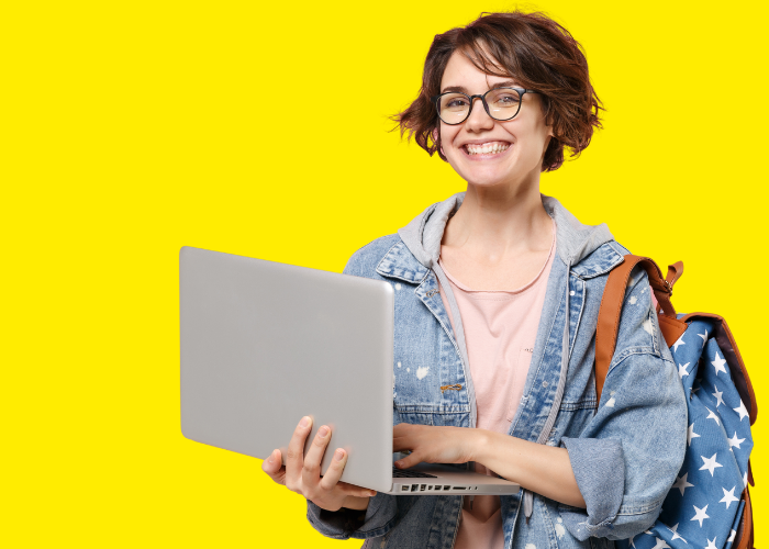 Eine junge Frau mit Laptop in der Hand und Rucksack auf dem Rücken schaut breit lächelnd in die Kamera.