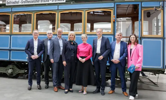 Frau Staatsministerin Ulrike Scharf, Herr Dr. Markus Schmitz, Keynote-Speakerin Steffi Burkhart und die führenden Vertreter der bayerischen Wirtschaftsverbände vor einer Tram und lächeln in die Kamera.