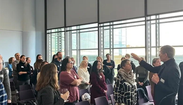 Ein Referent instruiert mehrere Workshopteilnehmende, die sich stehend im Raum positioniert haben