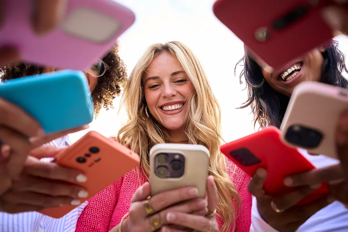 Mehrere Mädchen stehen im Kreis und schauen auf ihre Smartphones. Ein blondes Mädchen lächelt während sie auf ihr Smartphone schaut.